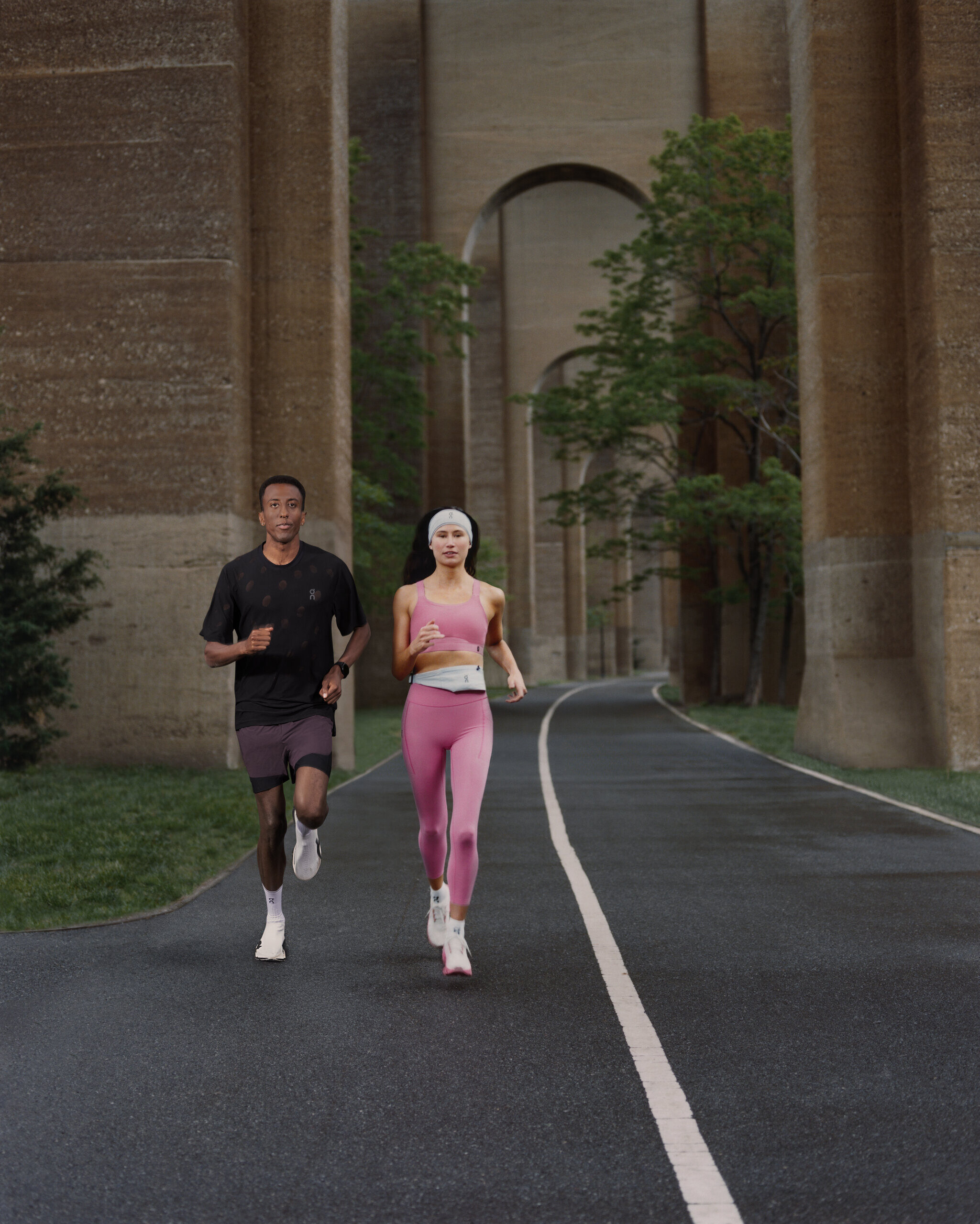 Two runners on a curving path beneath the tall concrete arches of a viaduct