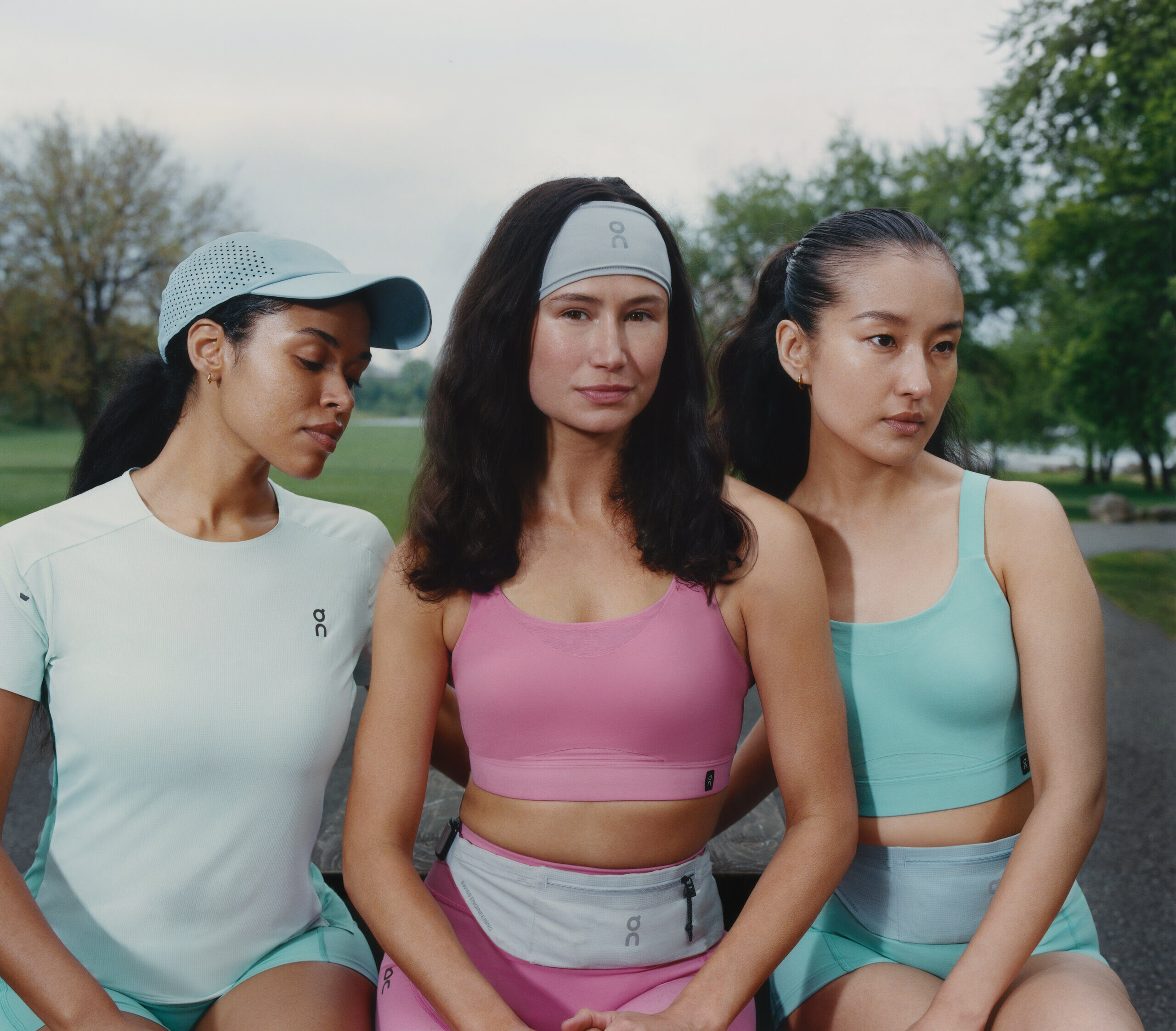 Three runners in pastel On kit sitting together on a bench in a park